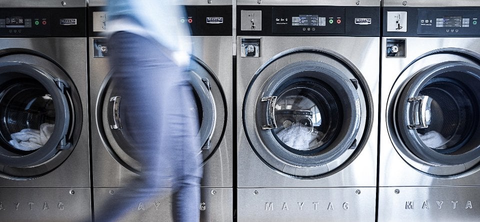 A row of Maytag Commercial washing machines in a commercial laundry environment.